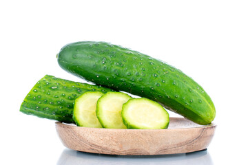 One whole ripe green cucumber and one cut into slices on a wooden saucer , macro, isolated on a white background.
