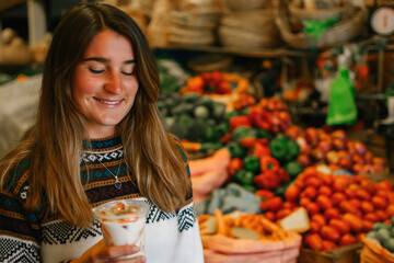 Portrait of a caucasian woman with jumper and smiling while holding a fruit salad and standing in the market