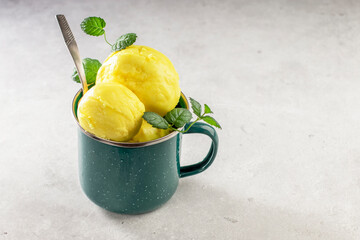 Balls of homemade mango ice cream with fresh mint in a metal mug on a light background. Natural nutrition. Copy space
