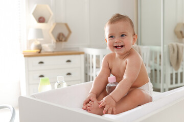 Cute little baby with bottle of massage oil on changing table at home