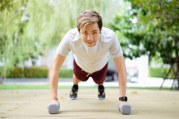 Active Asian sportsman making a body weight exercise, man doing push up workout with dumbbell. 