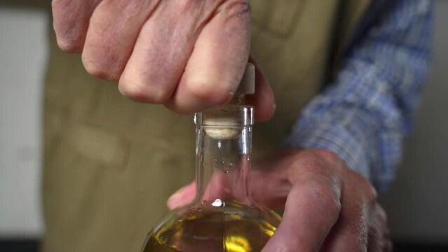 Old man is pressing cork into a filled glass bottle with his hands
