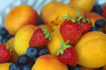 Naklejka na ściany i meble Apricots, strawberries and blueberries on a plate