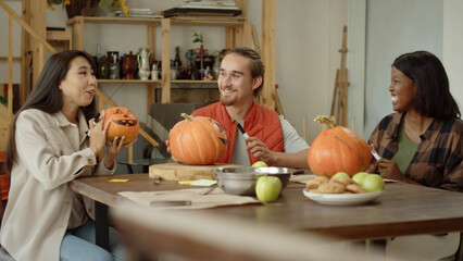 Friends are sitting at the table and talking about their painted halloween pumpkins
