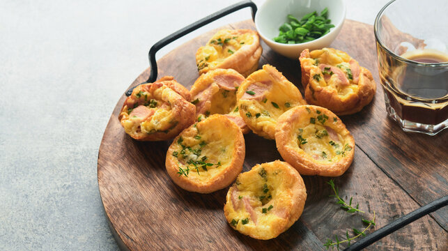 Delicious egg muffins with green onions, bacon, cheese and tomatoes on wooden board on light background. Healthy high protein and low carb breakfast. Homemade food.