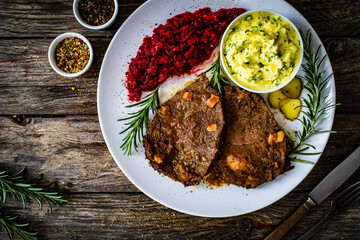 Roast stuffed beef with potato puree and red beets on wooden table

