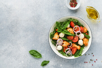 Panzanella, Italian Bread Salad. Traditional food of Italy with tomatoes, mozzarella balls, basil, onion and bread on light grey background. Traditional Italian cooking. Top view. Copy space.
