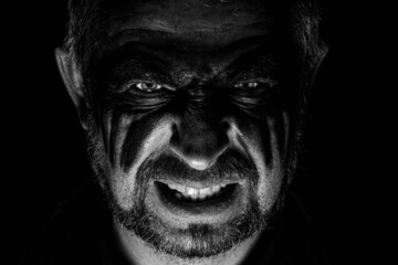 Viking man with a furious gaze and a painted face looks into the darkness with bright eyes