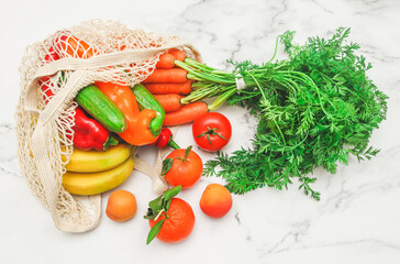 Seasonal vegetables and fruits: carrots, peppers, tomatoes, bananas, tangerines and apricots in a cotton mesh .