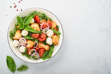 Panzanella Bread Salad. Traditional food of Italy with tomatoes, mozzarella balls, basil, onion and bread on light grey background. Traditional Italian cooking. Top view. Copy space.