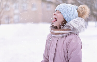 Fröhlicher Wintertag. Kleines Mädchen, das Schneeflocken isst. Kind, das draußen spielt und Schnee genießt.