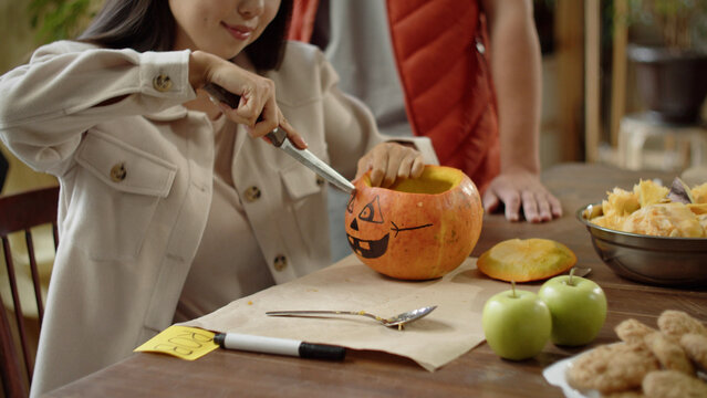 An adult girl starts carving eyes for a halloween pumpkin