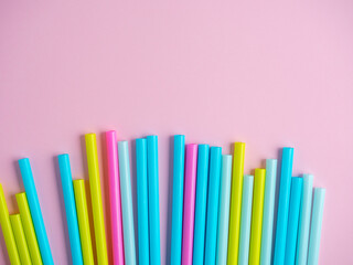 Close-up of multicolored plastic tubes on a pink paper background. Top view, flat lay