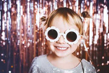 Portrait of happy little girl in dress and sunglasses having fun on the festive background. Kids birthday or fancy dress party, disco music or New Year. Celebration and Holiday concept.