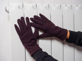 hands dressed in brown gloves are attached to a white central heating battery. The concept of heating devices. winter season. Side view