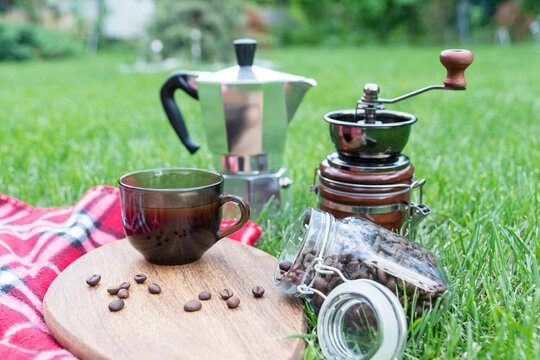 picnic on grass. Coffee cup, coffee beans, geyser coffee maker and coffee ginder on green summer grass. Outdoor relax.