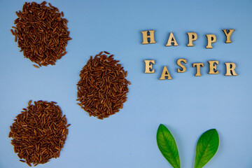 top view of the inscription from wooden letters happy easter, eggs from unpolished brown rice and rabbit ears from green leaves, proper and healthy nutrition, holiday diet