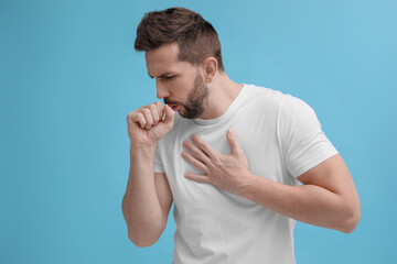 Man coughing on light blue background. Cold symptoms - obrazy, fototapety, plakaty