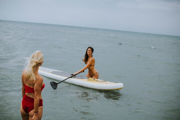 Two young women with paddle board in the sea on a summer day