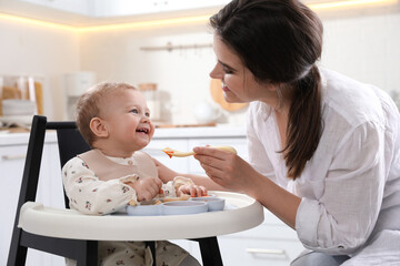 Mother feeding her cute little baby in kitchen