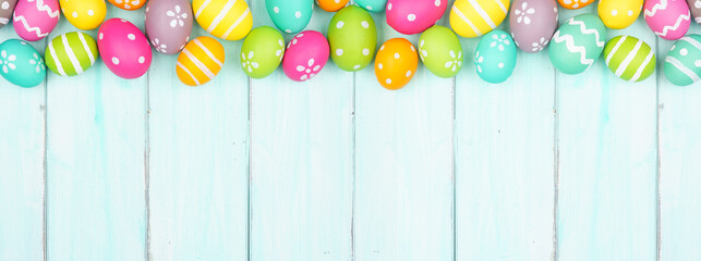Colorful Easter Egg top border over a soft blue wood banner background. Copy space.