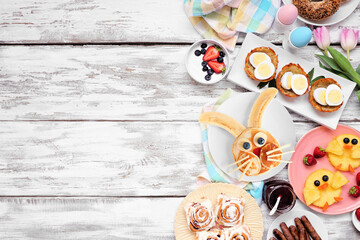 Fototapeta na wymiar Easter breakfast or brunch side border. Top view on a white wood background. Bunny pancake, egg nests, chick fruit and a collection of spring food items. Copy space.