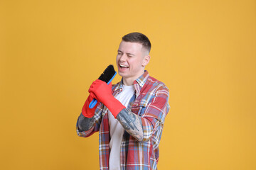 Handsome young man with brush singing on orange background