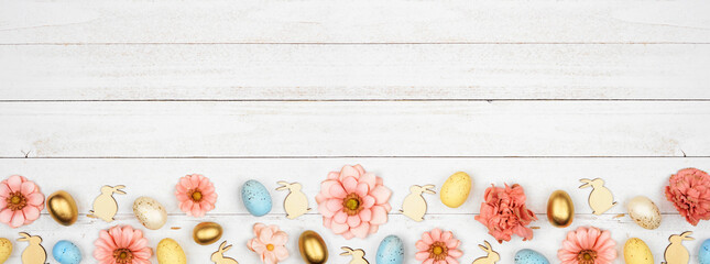 Easter bottom border with eggs, paper flowers and wooden bunnies. Top view against a white wood banner background. Copy space.