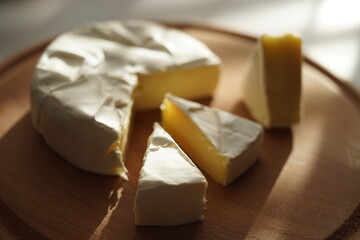 Camembert cheese with three slices triangles on a sunny wooden board
