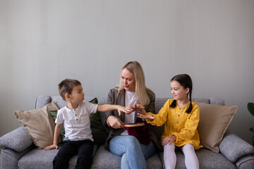 mom and kids are sitting on a gray sofa in the room and playing a game of magic tricks. Games with children at home