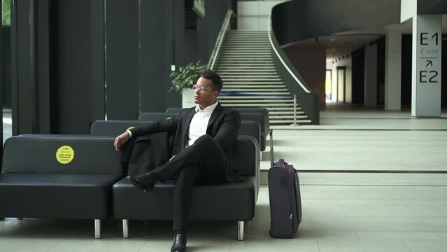 Young businessman or executive waiting for flight and sitting in airport lobby spbd. African American man looks with smile and thinks or dreams, waits for plane to fly off to business trip and sits at