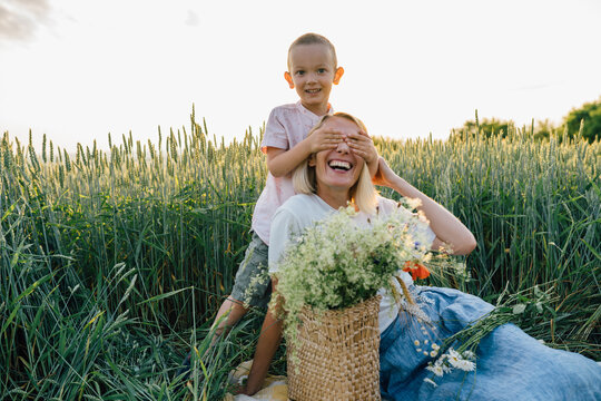 Enjoy life, having fun, leisure, relaxation, lifestyle concept. Family portrait of mother and little son, outdoors. Mom and child have fun play picaboo, sits on blanket at summertime.