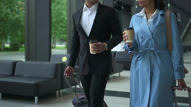 Successful businesspeople talking and walking with suitcases in hands in terminal or office spbd. Closeup view of American African businessman talks to beautiful woman and holds coffee cup, moves