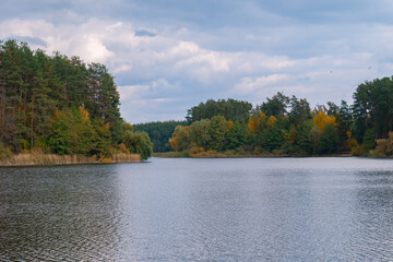 Scenic landscape of river, cloudy sky and trees, starting to get yellow in October