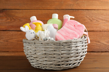 Wicker basket full of different baby cosmetic products, accessories and toys on wooden table