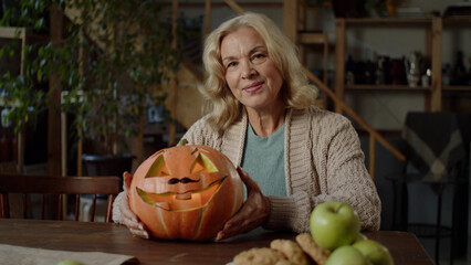 An elderly lady is holding a pumpkin and looking to the camera