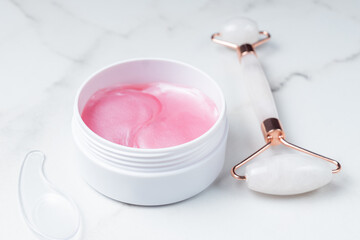 face massager roller made from natural stone and pink eye patches on marble background. Skin care treatment