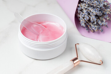 Pink hydrogel patches for skin under the eyes and rose quartz massage face roller on a table. Skin care home routine. Professional spa salon at home.