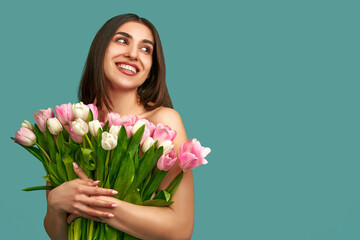 Portrait of a beautiful young woman on a blue background holding a bouquet of white and pink tulips. Spring and beauty concept.