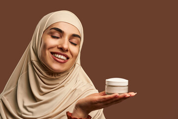 Portrait of beautiful modern muslim woman with natural make-up dressed in beige hijab smiling with...