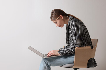 Woman with bad posture using laptop while sitting on chair against light grey background, space for...