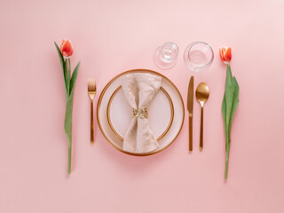 Festive pink table setting. Pink plate with gold cutlery and red tulip on pink background. Aesthetic stylish dinner table setting for Women's day, Mother's Day, wedding or anniversary. Flatlay topview