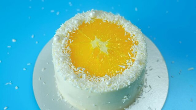 Cake with orange and coconut shavings spinning on a blue background.