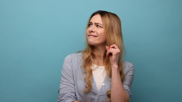 Portrait of thoughtful upset woman pondering serious issues, looking with uncertain hesitant expression, making difficult choice, wearing striped shirt. Indoor studio shot isolated on blue background.