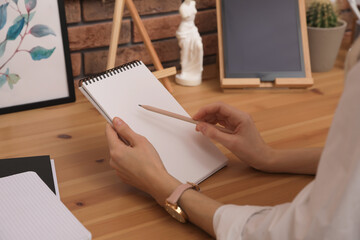 Woman drawing in sketchbook with pencil at wooden table indoors, closeup