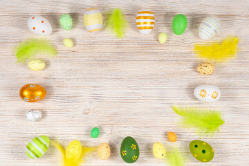 Easter frame with eggs and feathers on a light wooden background. Minimal concept. View from above. Card with copy space for text.