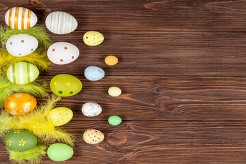 Fototapeta na wymiar Happy Easter concept. Colorful Easter eggs with bright feathers on a dark wooden background. View from above. Place for inscription, text. Basis for a postcard.
