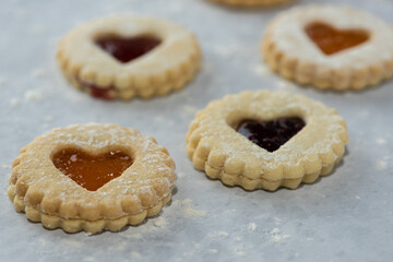 Elevated front view of homemade heart shaped jam filled holiday or celebration cookies with scattered flower on a marble table. 
