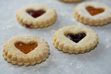 Elevated front view of homemade heart shaped jam filled holiday or celebration cookies with scattered flower on a marble table. 