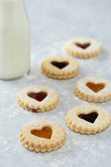 Vertical image of Heart shaped Valentines day or holiday homemade cookies with different jams  and jar of milk in the background from an elevated front angle on a marble table.